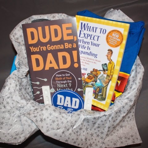 In the basket: 2 Daddy Books, 2 T-Shirts (The Man Behind The Bump & Super Dad), Dad To Be Pin & 2 Positive Pregnancy Tests.